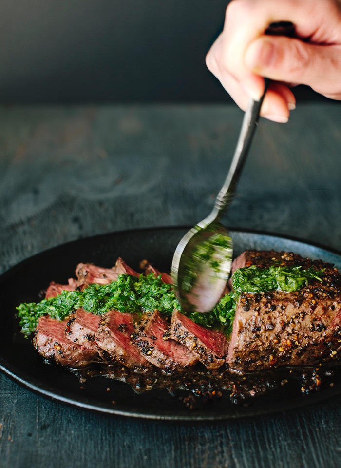 Sliced peppercorn crusted steak drizzled in chimichurri sauce in a cast iron skillet Sliced peppercorn crusted steak drizzled in chimichurri sauce in a cast iron skillet