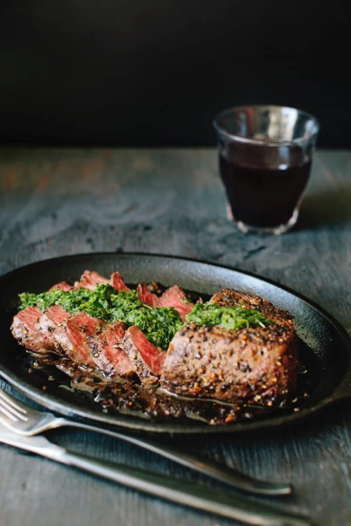 Cast iron skillet with steak chimichurri and a glass of red wine on a rustic table Cast iron skillet with steak chimichurri and a glass of red wine on a rustic table