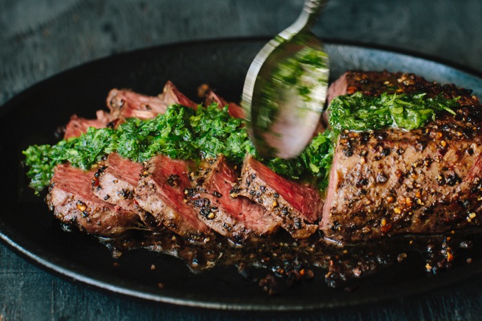 Sliced steak drizzled in chimichurri sauce in a cast iron skillet Sliced steak drizzled in chimichurri sauce in a cast iron skillet