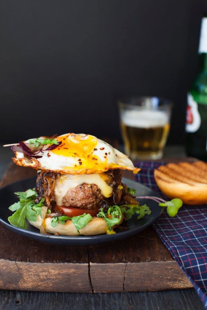 Breakfast Fried Egg Burger on a Wooden Table with a Glass of Beer Breakfast Fried Egg Burger on a Wooden Table with a Glass of Beer